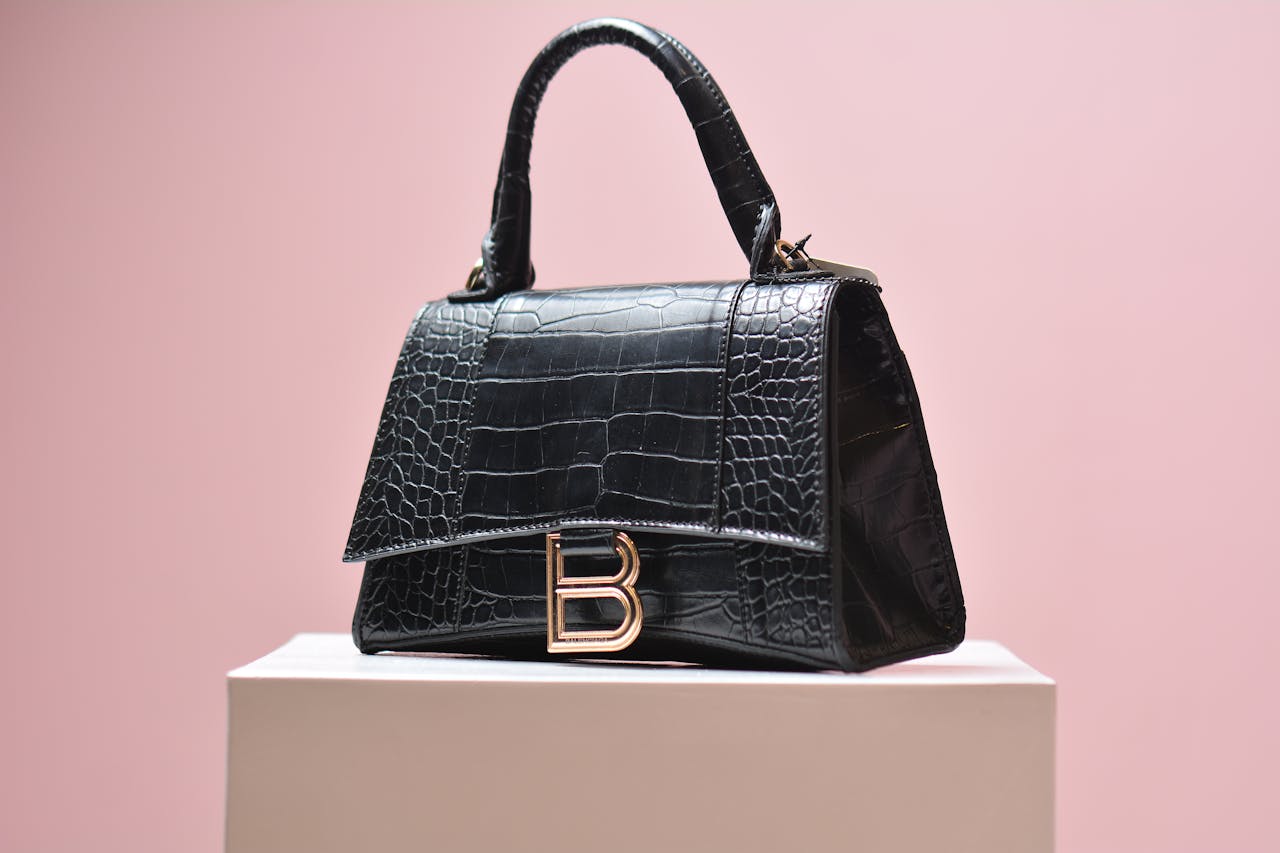Elegant black leather handbag with textured design on a pink background, perfect for high-end fashion shoots.